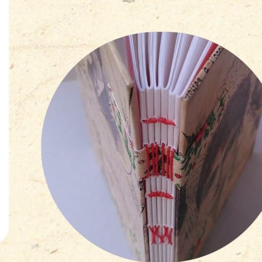 Gros plan sur la tranche d'un carnet relié en reliure couture sur rubans avec couture apparente sur rubans rouges - Cosette Cartonera
